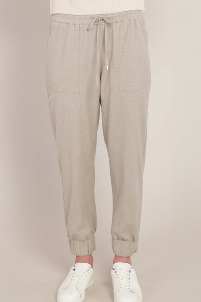 Beige jogger pants worn with white sneakers on a beige background