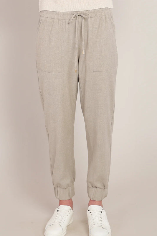 Beige jogger pants worn with white sneakers on a beige background