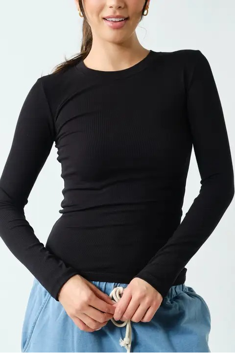 A woman wearing a fitted black long-sleeve ribbed top and light blue drawstring pants, photographed against a plain light background.