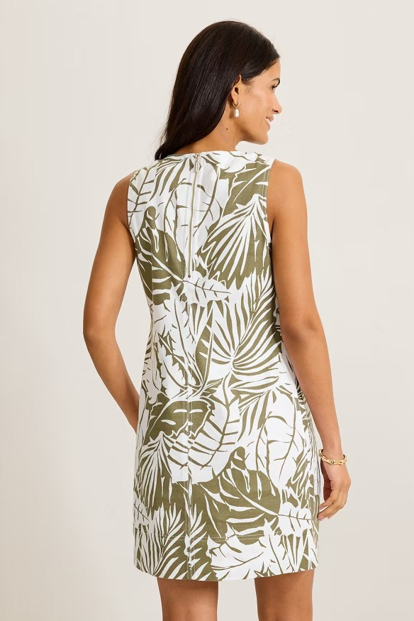 Woman wearing a sleeveless dress with leaf pattern on a plain background