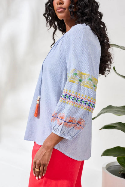 Woman wearing a light blue top with colorful patterns and red pants against a white background