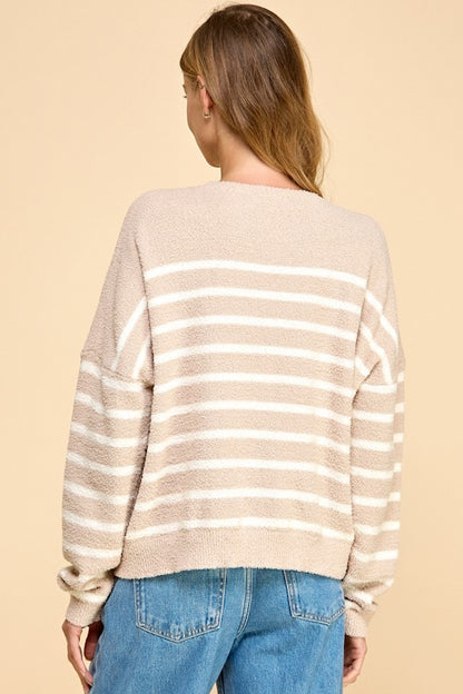 A woman shown from the back wearing a fuzzy knit sweater with horizontal beige and white stripes, paired with blue jeans, against a solid beige background.