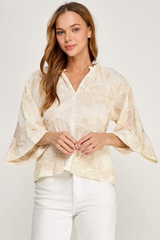 Woman wearing a beige lace blouse and white pants on a plain background