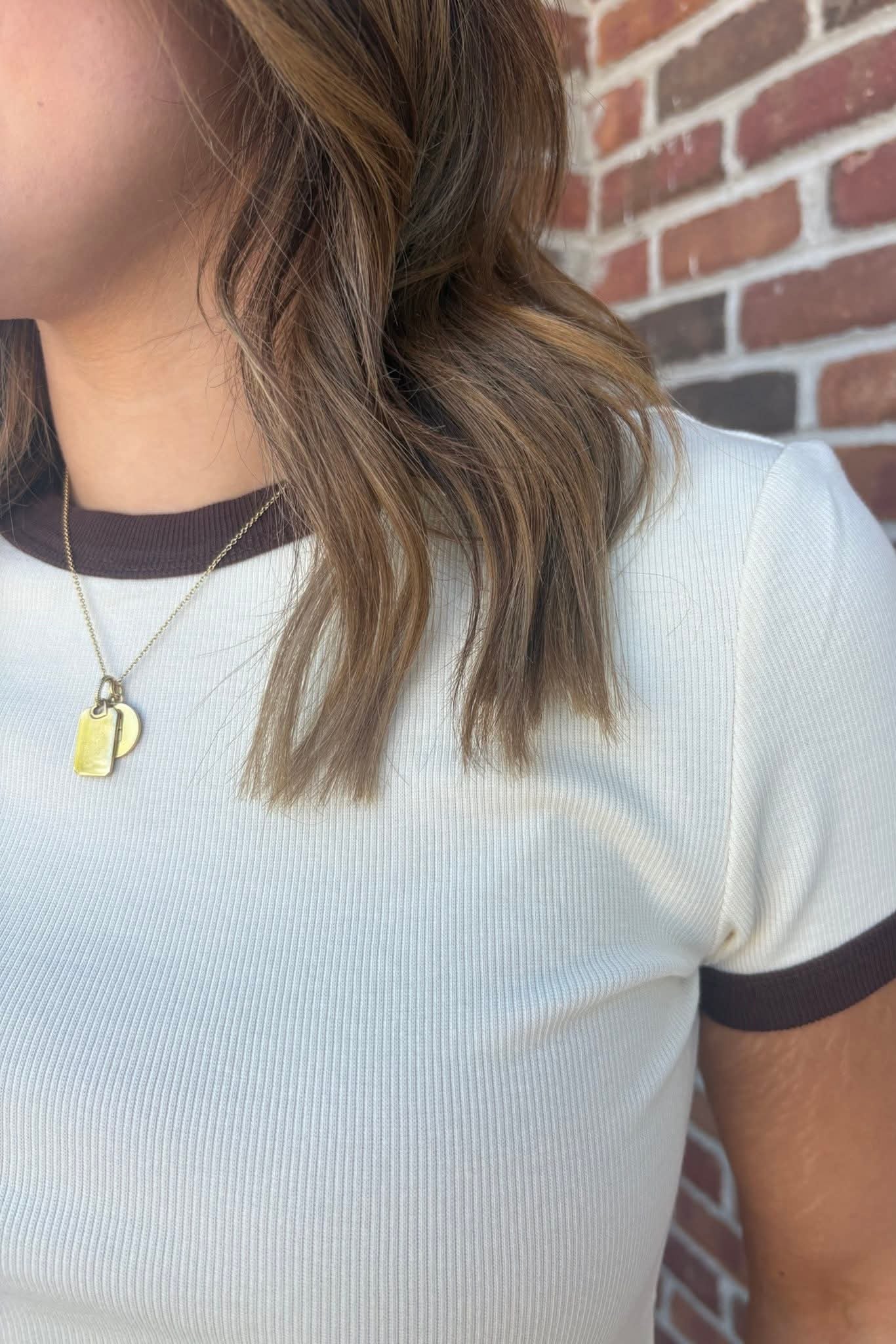 Person wearing a white shirt with brown trim against a brick wall