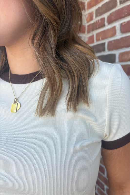 Person wearing a white shirt with brown trim against a brick wall