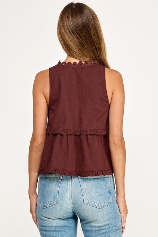 A woman shown from the back wearing a sleeveless burgundy top with a scalloped neckline and ruffled hem, paired with light blue jeans, against a plain white background.