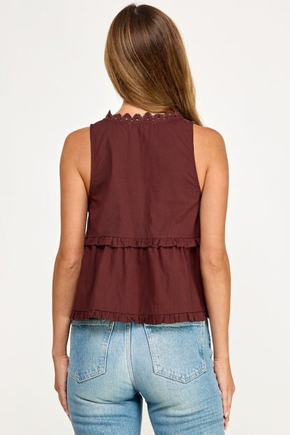 A woman shown from the back wearing a sleeveless burgundy top with a scalloped neckline and ruffled hem, paired with light blue jeans, against a plain white background.