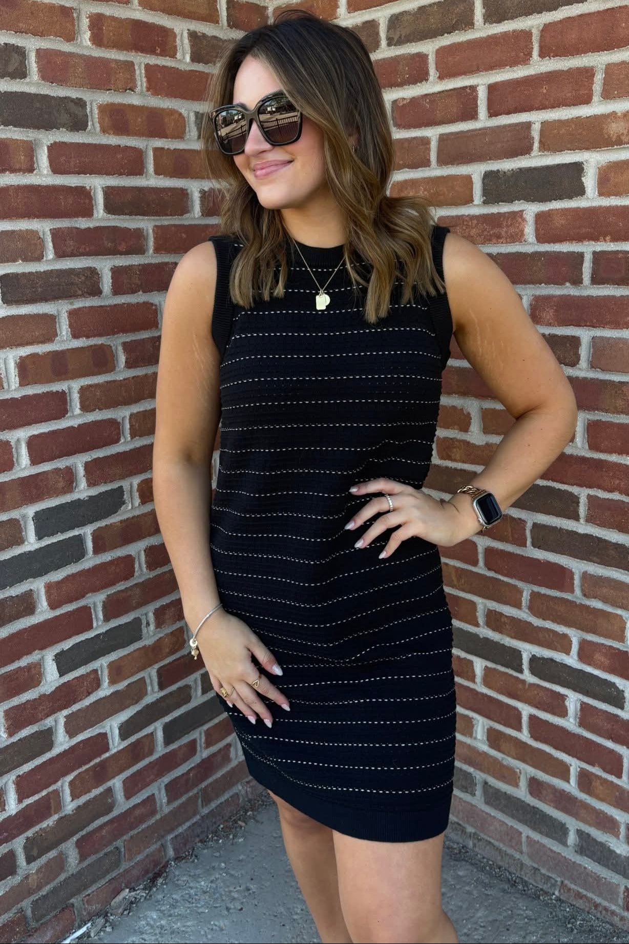 Woman in a black dress standing against a brick wall