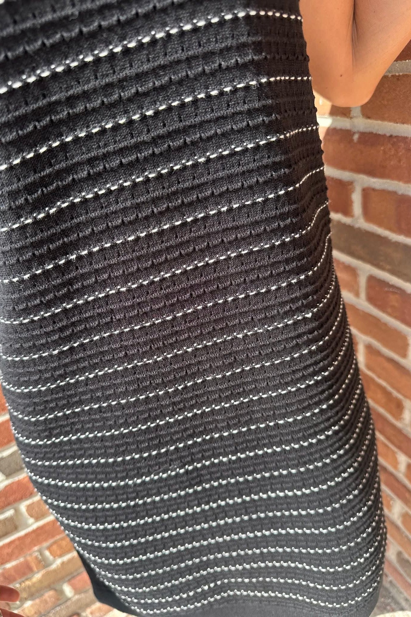 Close-up of a person wearing a black and white striped shirt against a brick wall.