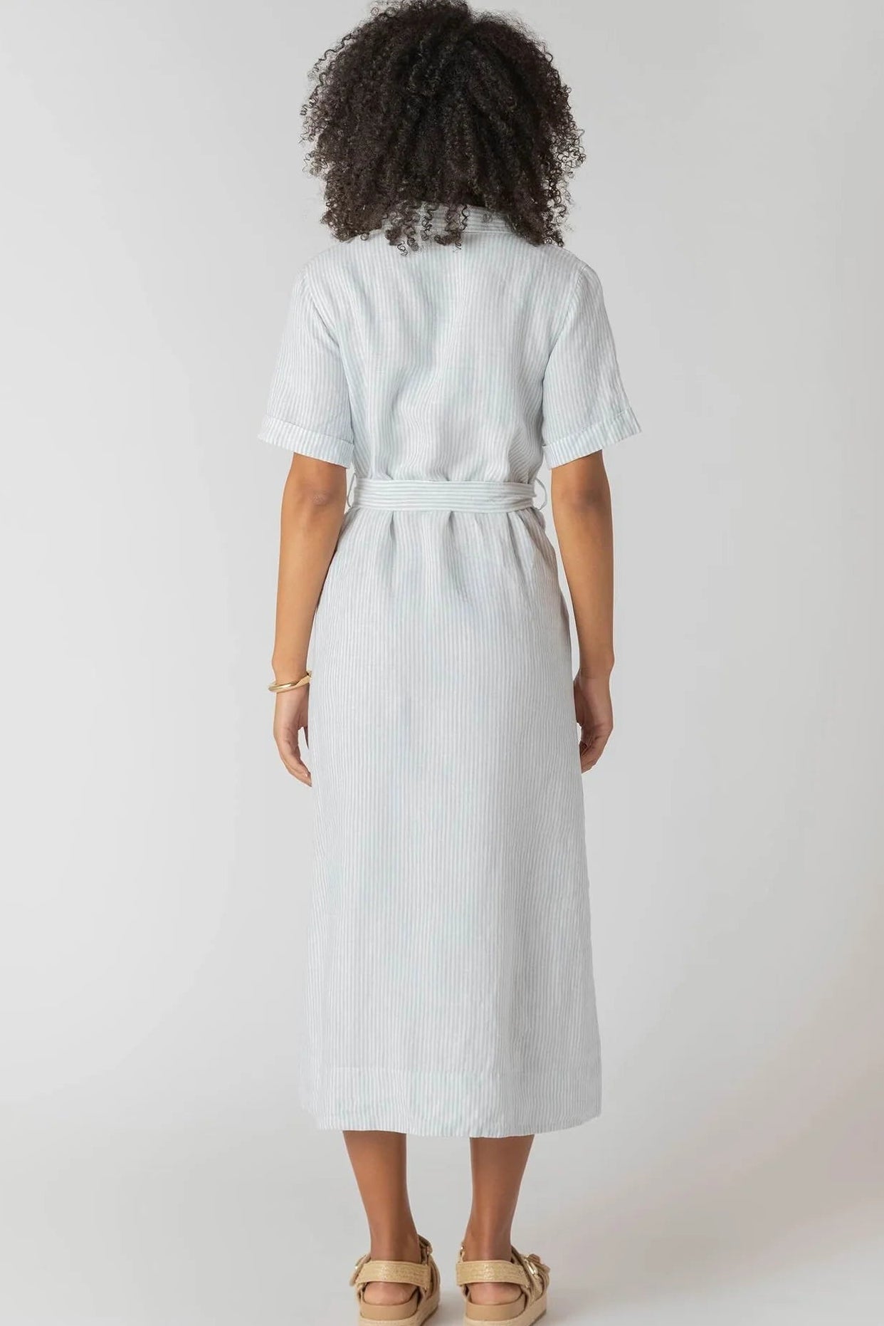 Person wearing a light blue dress with a belt on a white background