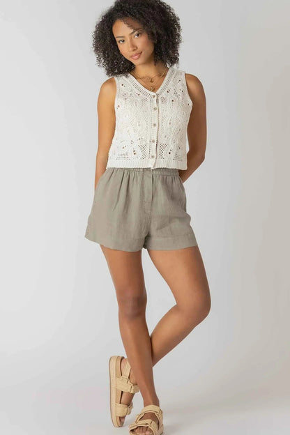 Woman wearing a white sleeveless top and green shorts on a plain background