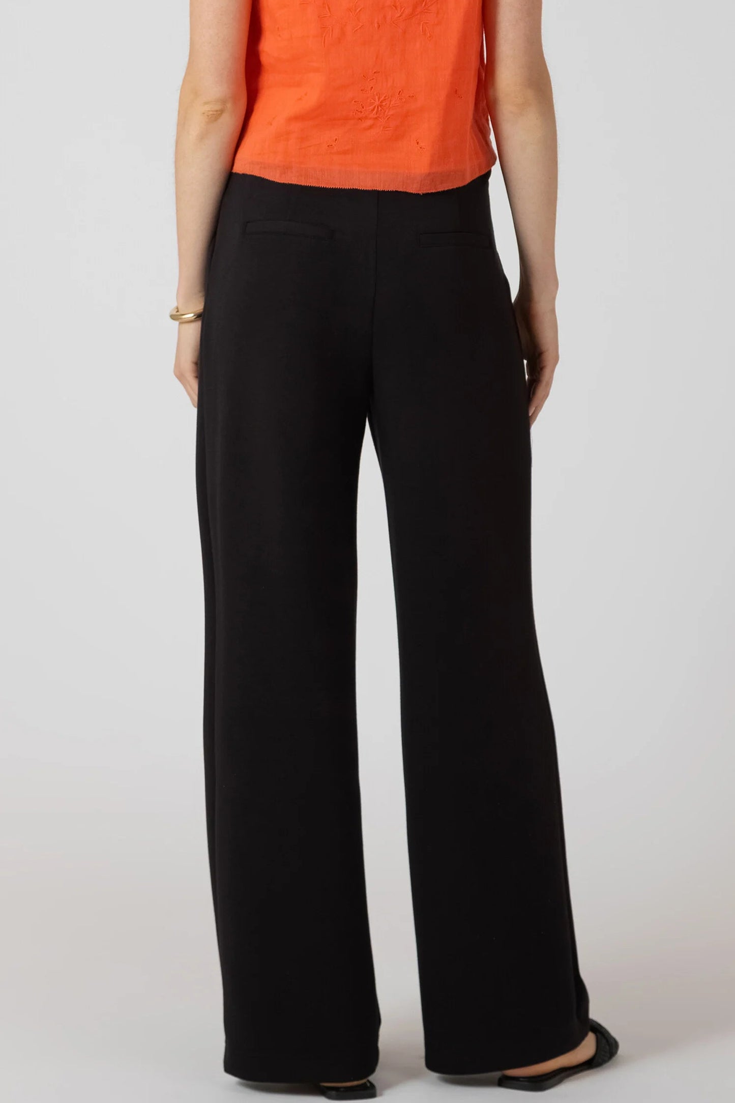 Person wearing black wide-leg pants and an orange top on a white background