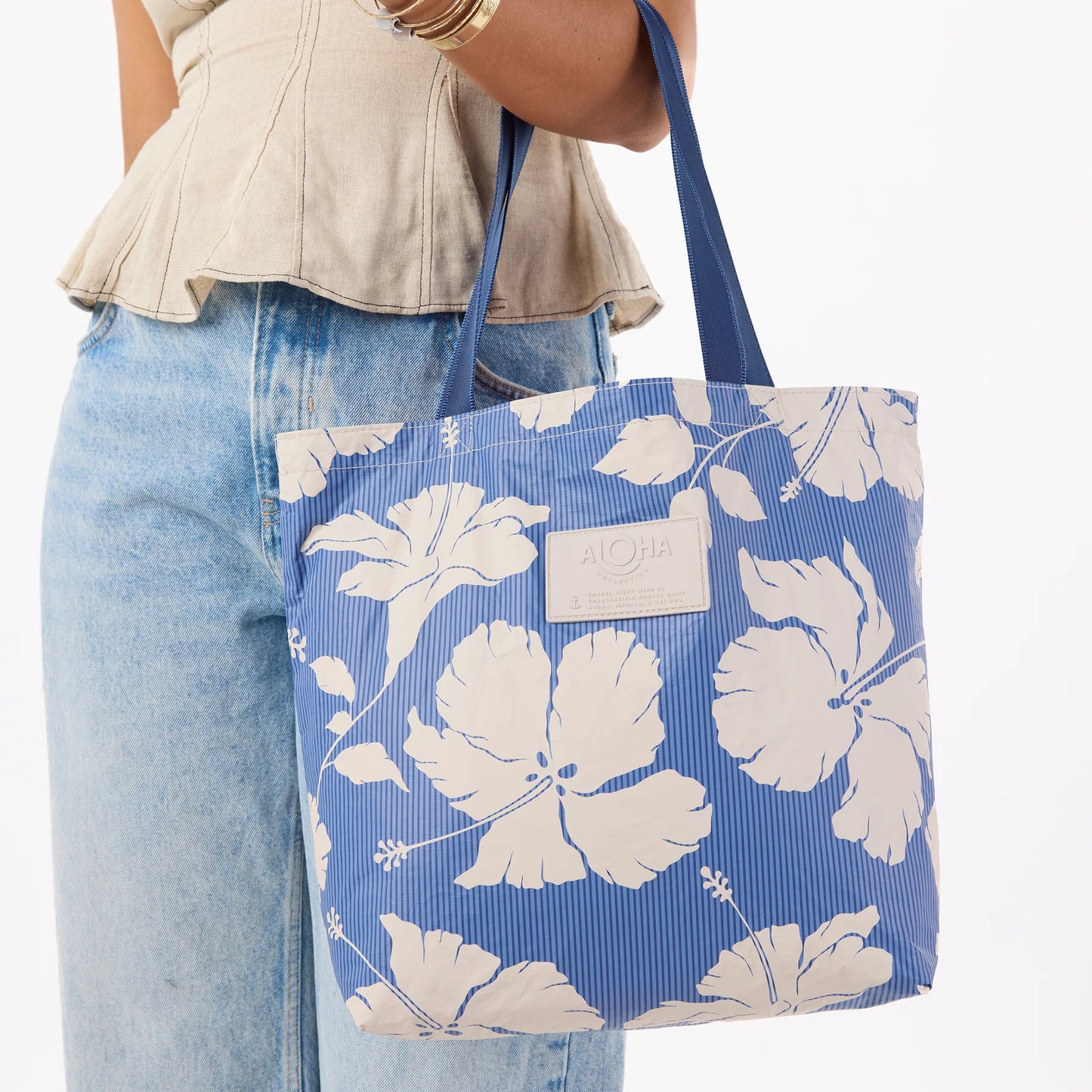 Blue tote bag with white floral pattern held by a person wearing jeans and a beige top.