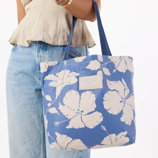 Blue tote bag with white floral pattern held by a person wearing jeans and a beige top.
