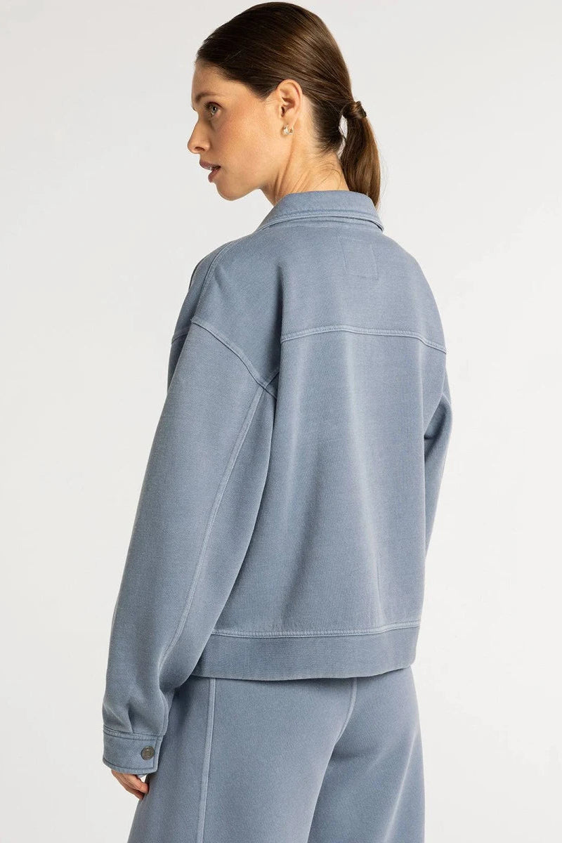 A woman shown from the back wearing a light blue denim jacket and matching light blue denim pants against a plain white studio background.
