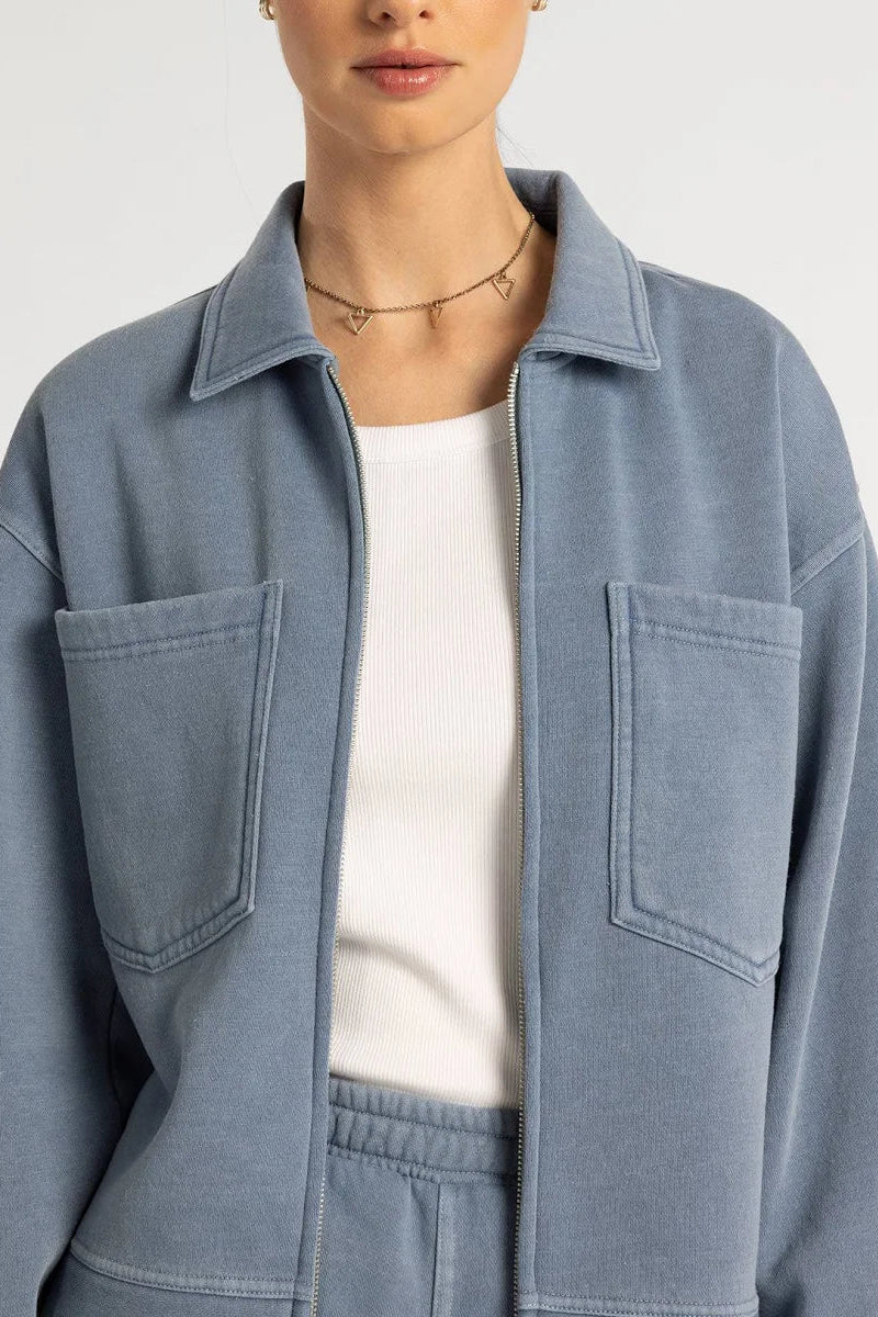 Person wearing a light blue denim jacket over a white shirt on a plain background