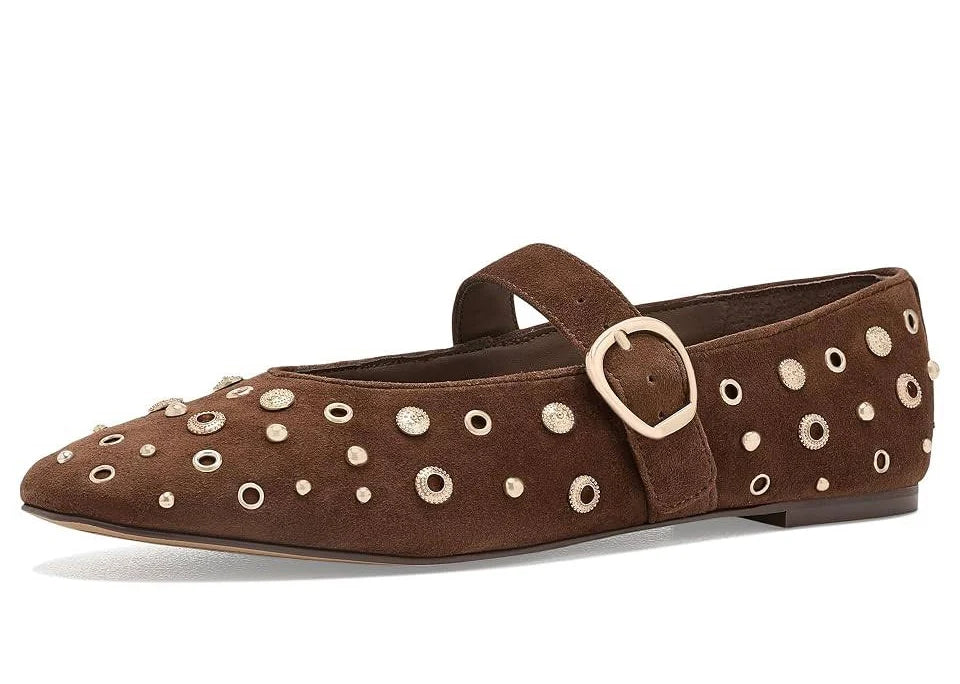 A brown suede flat shoe with a strap and buckle, decorated with metallic silver studs and eyelet details, shown against a plain white background.
