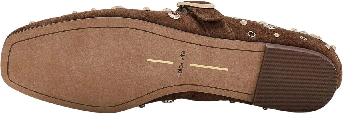 A close-up bottom view of a brown suede loafer with silver studs and eyelets, showing the tan outsole with the 'dolce vita' brand name printed in black.