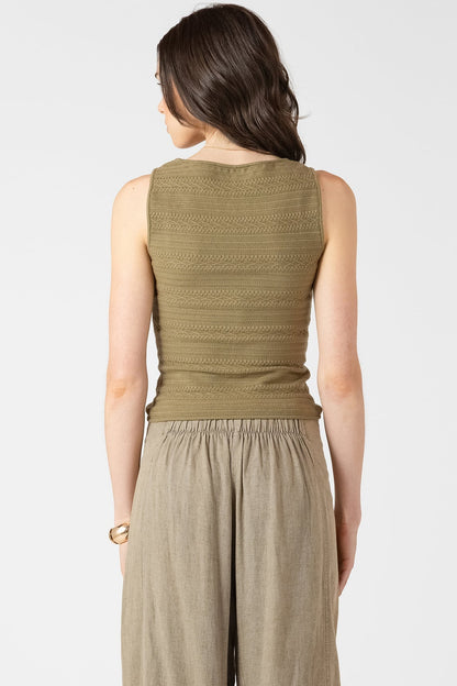 Woman wearing a green sleeveless top and beige pants on a white background