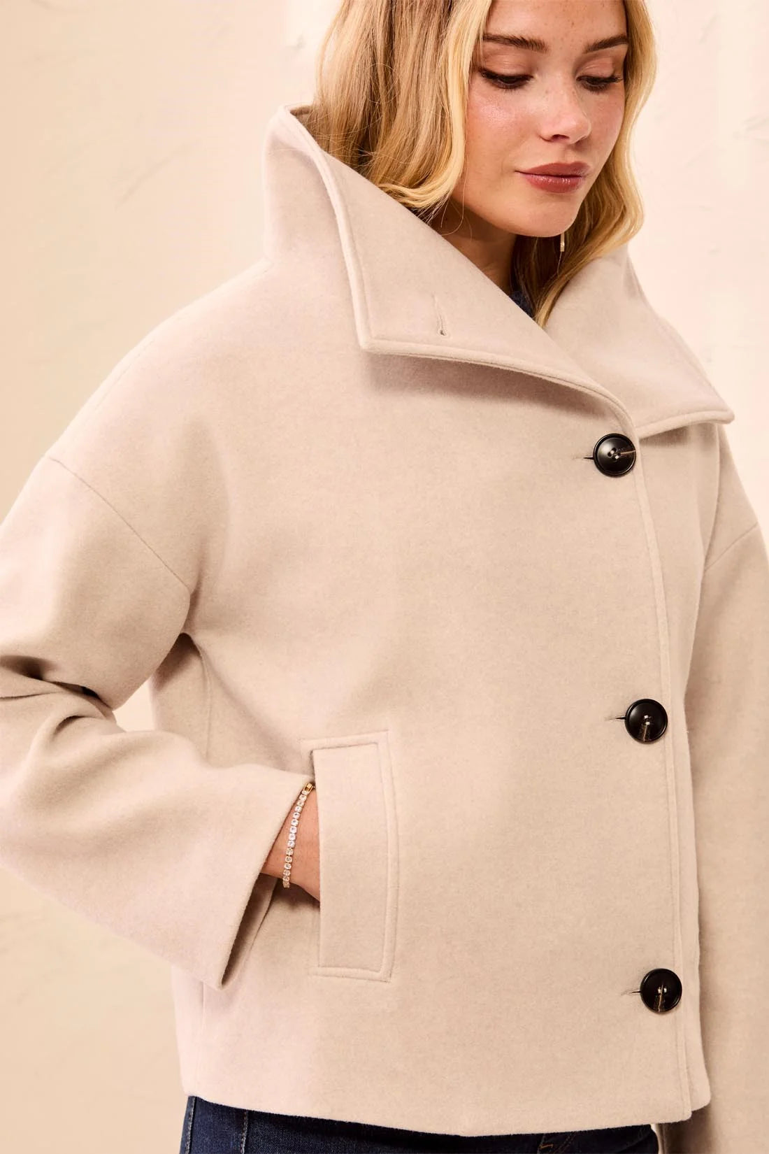 Woman wearing a beige coat with black buttons on a plain background