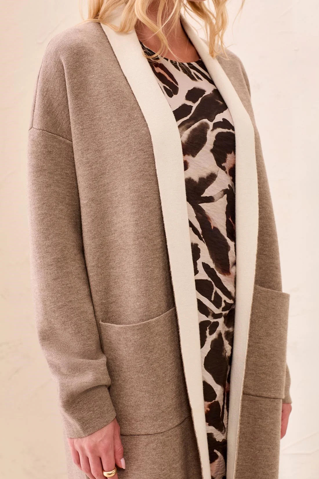 A woman wearing a taupe open-front cardigan with a contrasting cream collar and cuffs, layered over a brown and beige animal print dress.