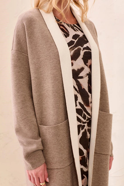 A woman wearing a taupe open-front cardigan with a contrasting cream collar and cuffs, layered over a brown and beige animal print dress.