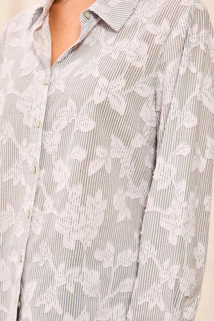 Close-up of a button-front collared shirt with a fine vertical stripe pattern in light gray and white, overlaid with a white floral lace or embroidered pattern.