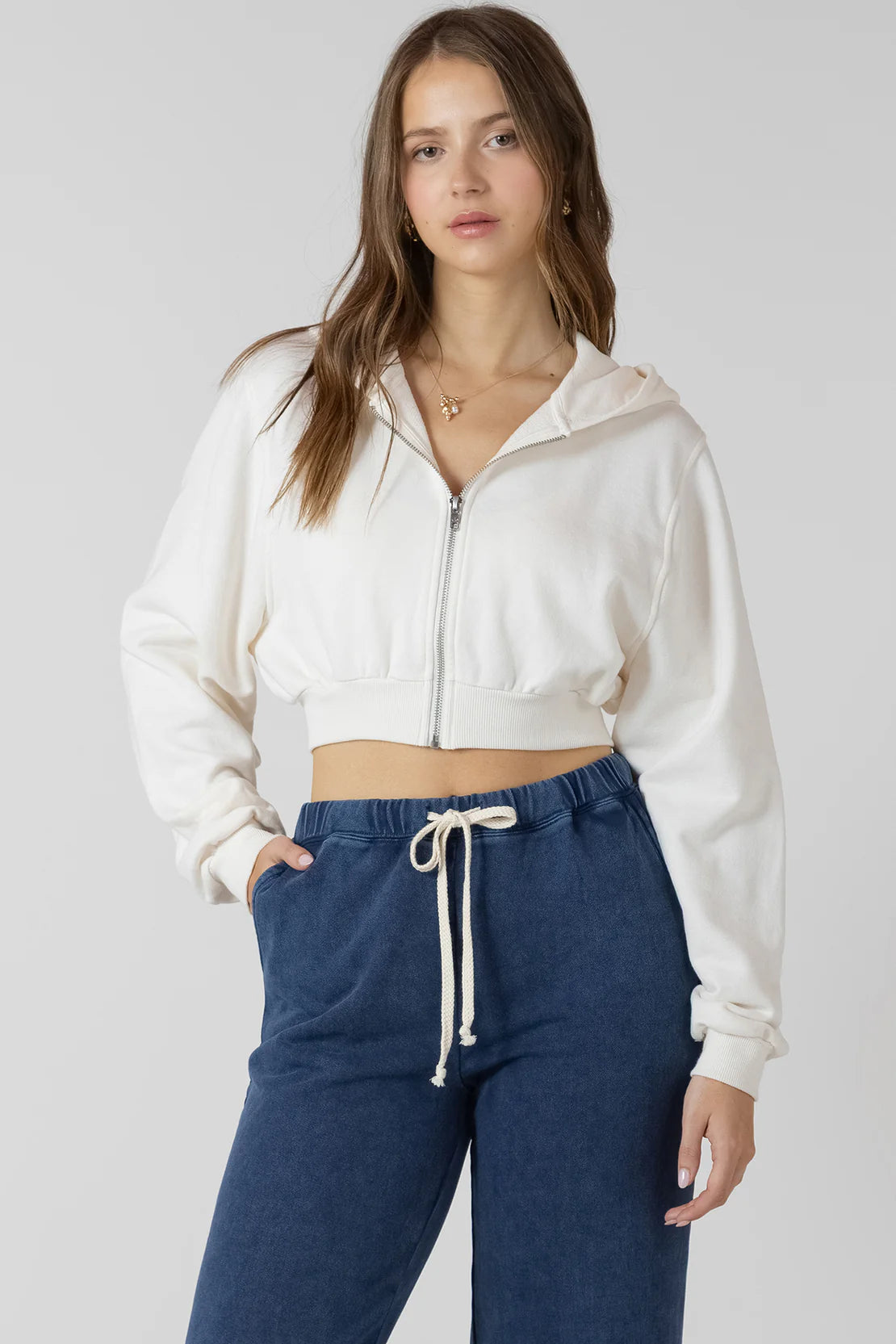 Woman wearing a white zip-up hoodie and blue pants on a plain background