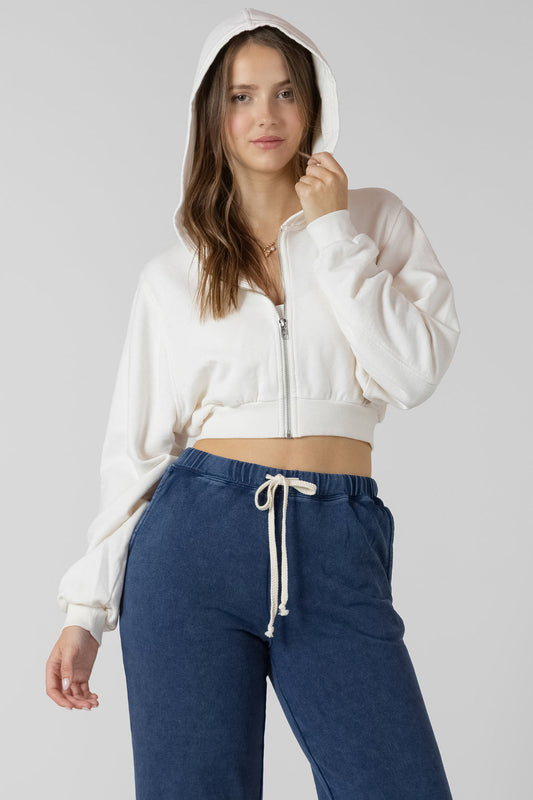 Woman wearing a white cropped hoodie and blue pants on a gray background