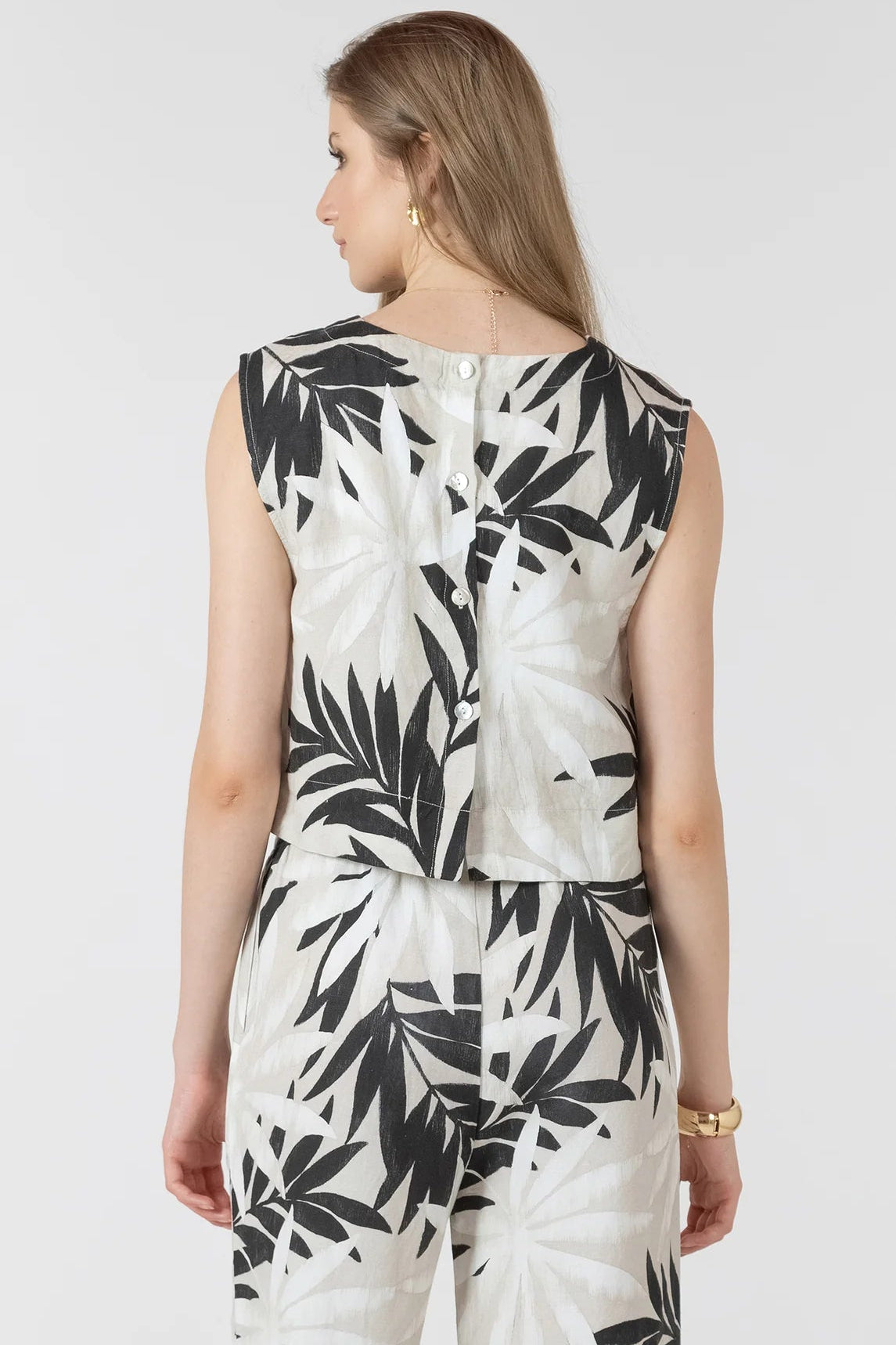 Woman wearing a white outfit with black leaf pattern on a plain background