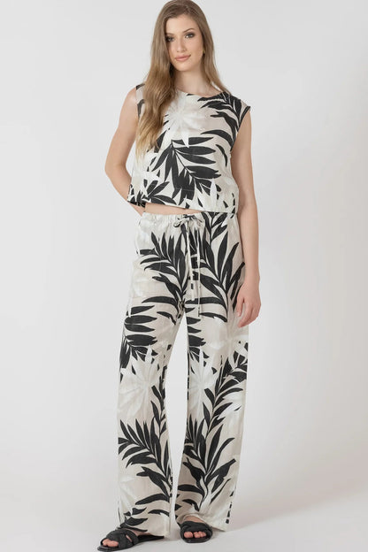 Woman wearing a sleeveless top and pants with black leaf pattern on a white background