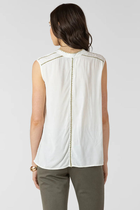 Woman wearing a white sleeveless top with decorative elements on a plain background