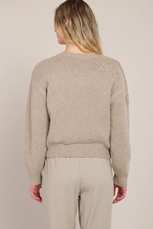 Person wearing a beige sweater and pants against a plain background