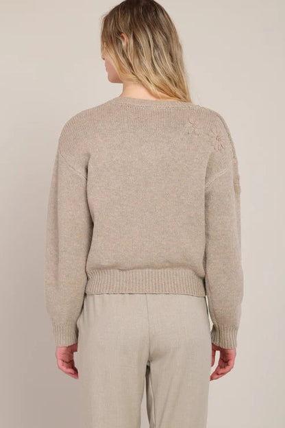 Person wearing a beige sweater and pants against a plain background