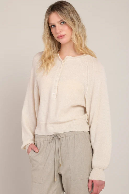 Woman wearing a beige sweater and pants against a plain background