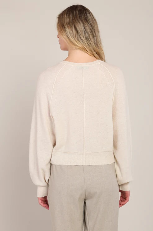 Person wearing a beige sweater and pants against a neutral background