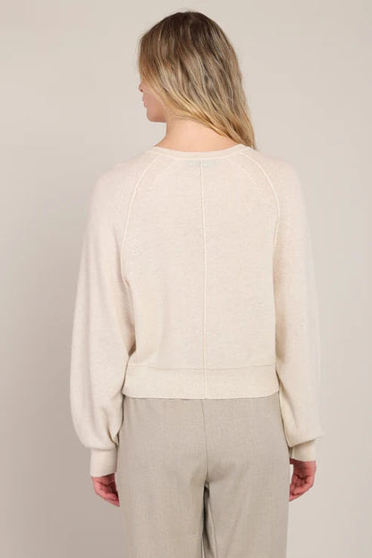 Person wearing a beige sweater and pants against a neutral background