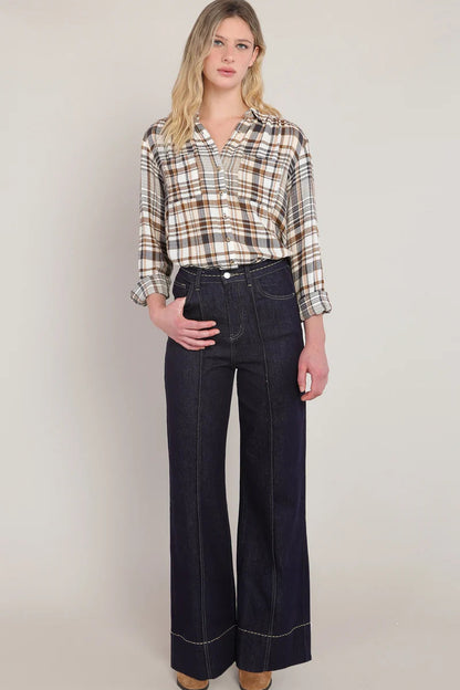 Woman wearing a plaid shirt and dark jeans against a plain background