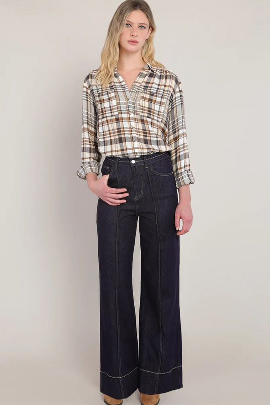 Woman wearing a plaid shirt and dark jeans against a plain background