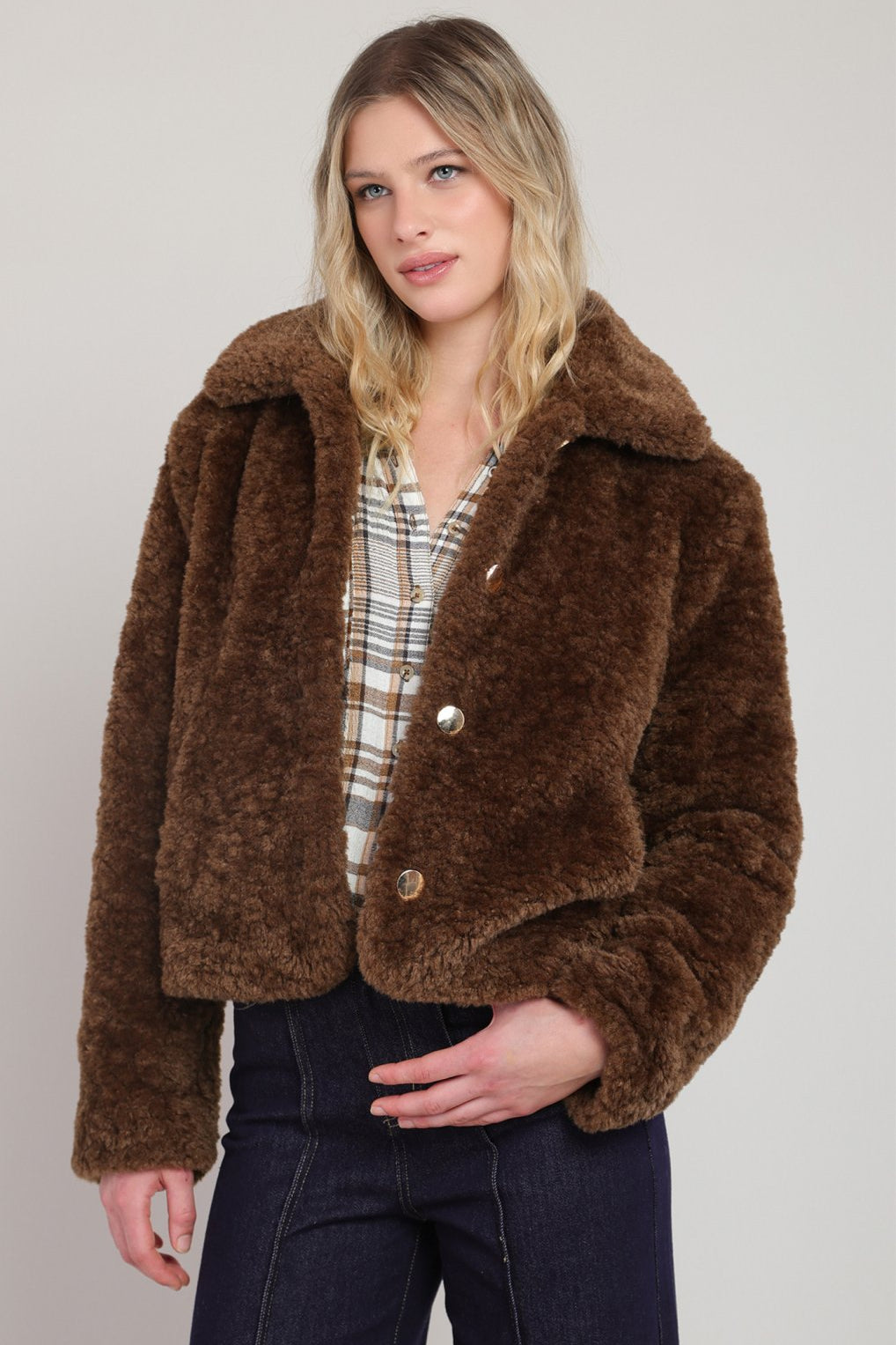 Woman wearing a brown faux fur jacket against a plain background