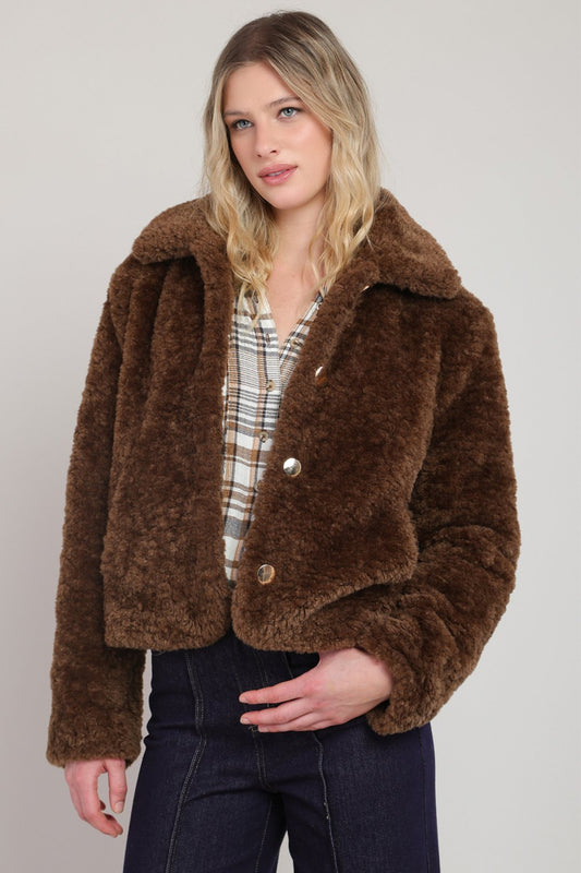 Woman wearing a brown faux fur jacket against a plain background