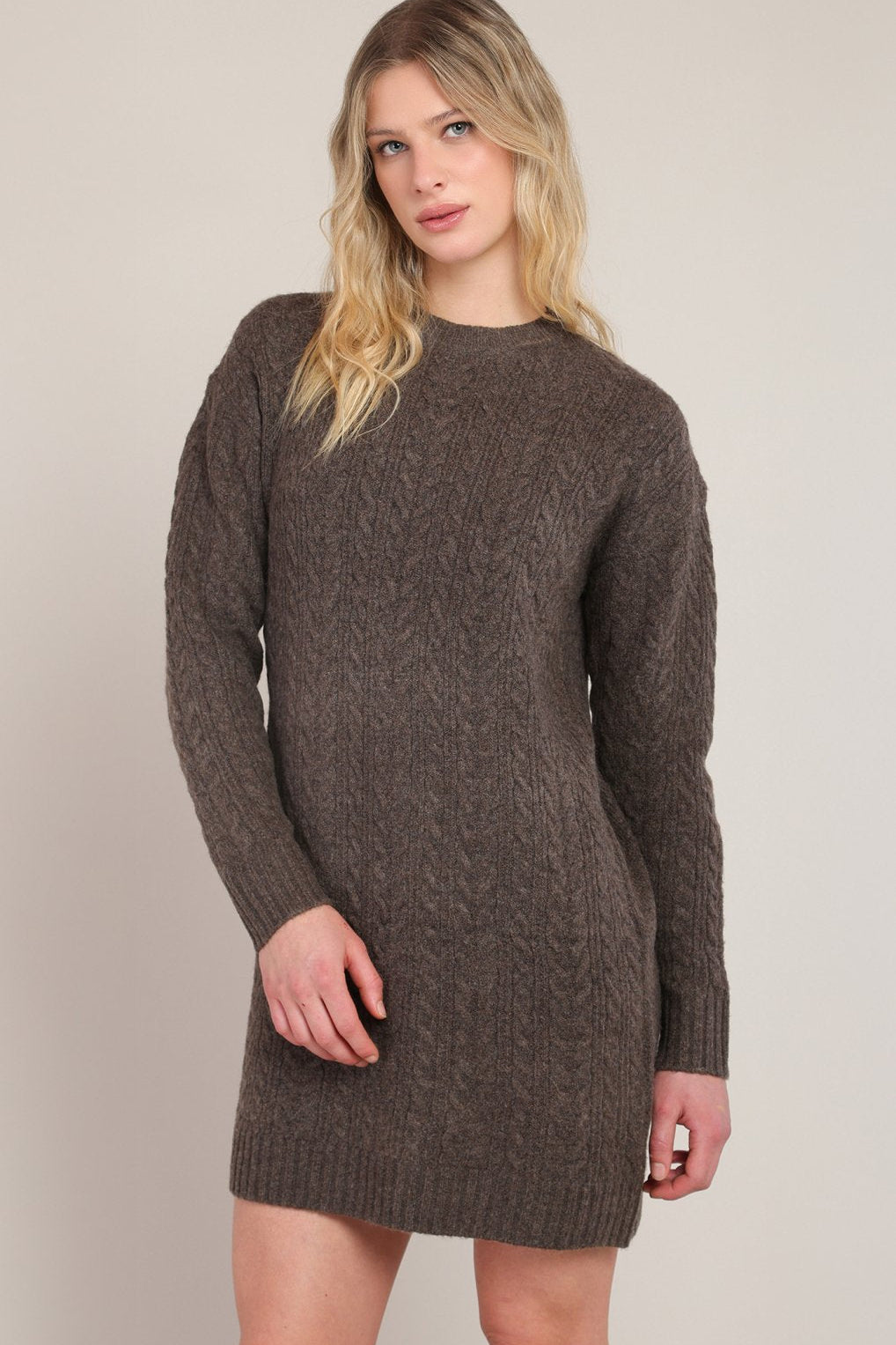 Woman wearing a brown knitted dress against a plain background