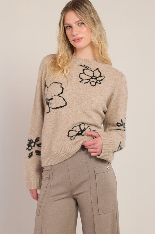 Woman wearing a beige sweater with black floral patterns on a plain background