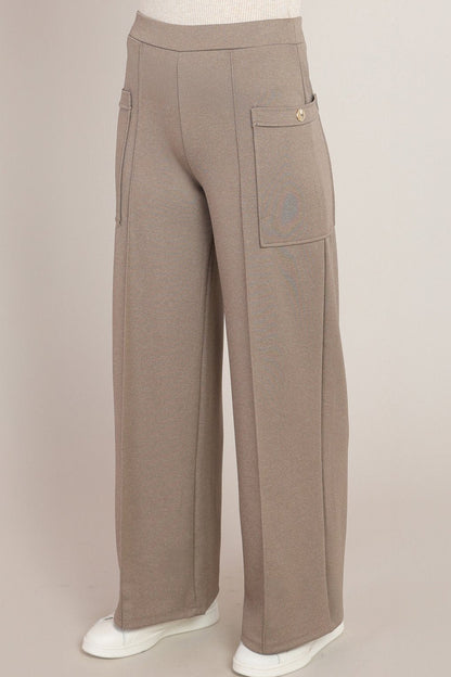 A pair of wide-leg taupe pants displayed on a mannequin lower body, featuring a high waist, side cargo pocket with a gold button, and white sneakers against a solid light beige background.