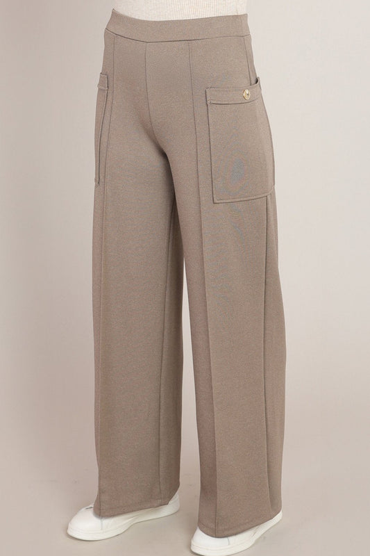 A pair of wide-leg taupe pants displayed on a mannequin lower body, featuring a high waist, side cargo pocket with a gold button, and white sneakers against a solid light beige background.