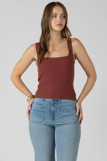Woman wearing a rust-colored tank top and light blue jeans on a plain background