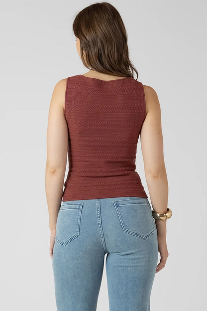 Woman wearing a rust-colored sleeveless top and light blue jeans on a plain background