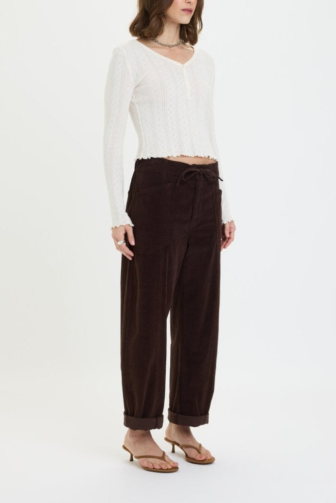 Woman wearing a white long-sleeve top and brown pants on a white background