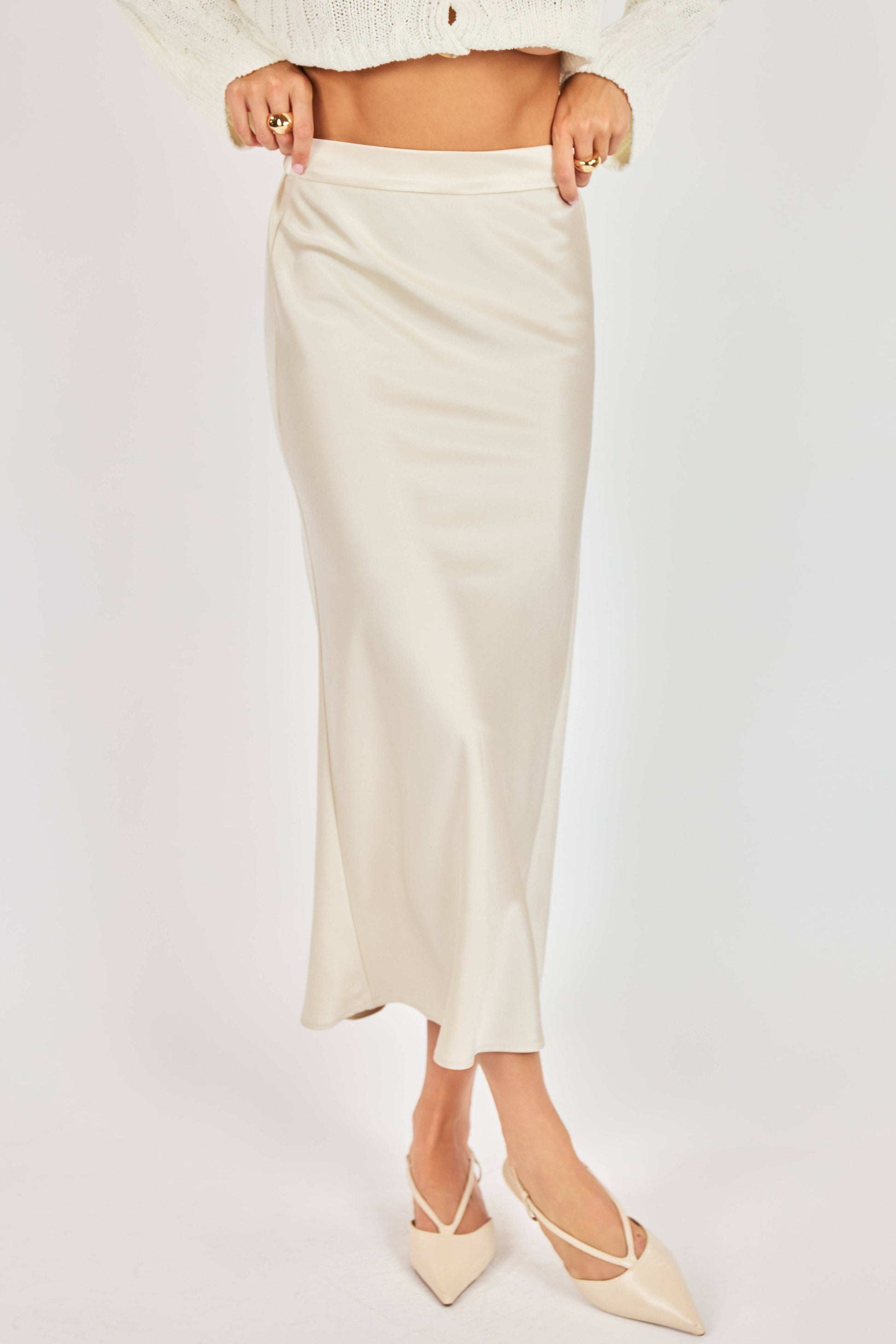 Person wearing a white skirt and beige shoes on a light gray background