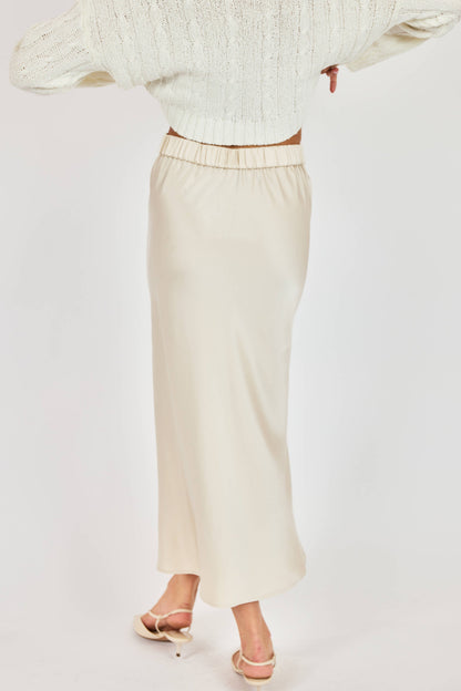 Person wearing a light-colored sweater and skirt on a plain background